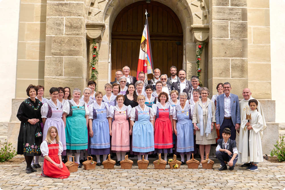 On voit le chœur mixte de Rossens en costume d'époque, posant devant l'église de Rossens à l'occasion de la célébration de la nouvelle bannière en 2023